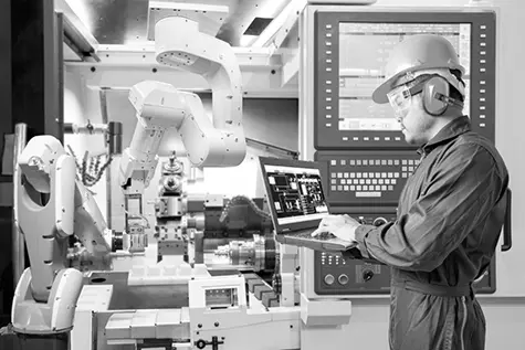 Male engineer with safety helmet and protective goggles working automatic robotic arm in factory