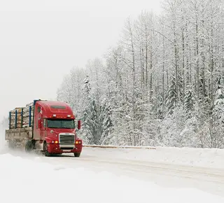 Logging transporter carrying tree trunks along snow covered frozen mountain road.