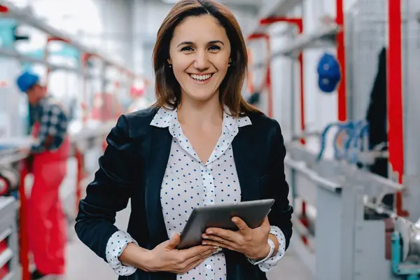 Smiling female machine vision supervisor holding a tablet with brightly lit facility blurred in background