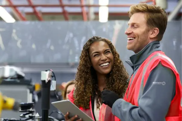 Female and male co-workers laughing together in a robotics factory