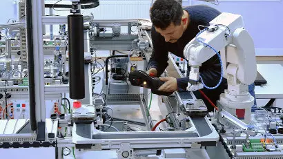 Male technician programming a collaborative robot (cobot) robotic arm with a control panel that is integrated on smart factory production line