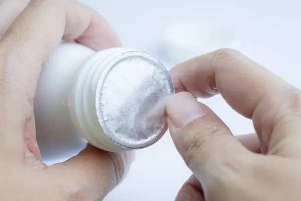 Female hands removing foil tamper from white bottle
